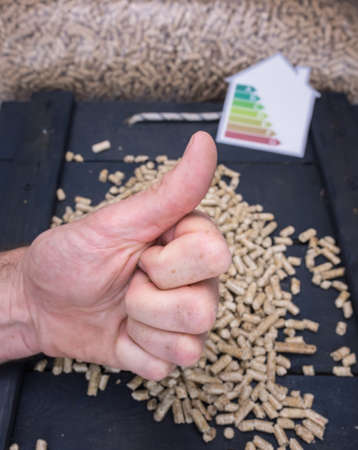 mans hand giving a thumbs up sign with wood pellet store and energy lable behindの写真素材