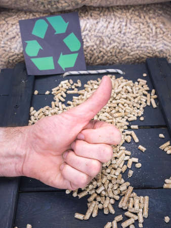 mans hand gives thumbs up with wood pellet store and recycling label behindの写真素材