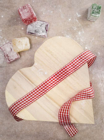 closeup of colourful turkish delight  with a rustic wooden heart shaped presentation box wrapped with a red and white  ribbon with brown work surface behindの写真素材
