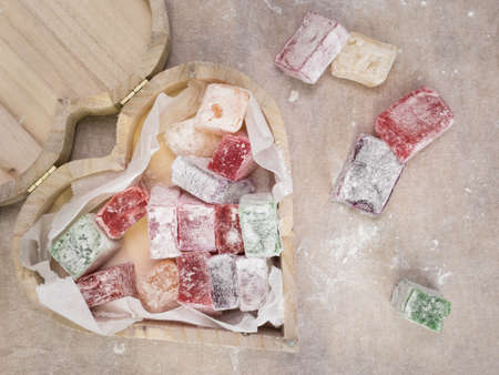 rustic heart shaped wooden box containing colourful turkish delight with turkish delight and brown work surface behindの写真素材