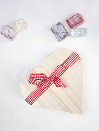 colourful turkish delight  with a rustic wooden heart shaped presentation box tied with a red and white  ribbon with white surface behindの写真素材