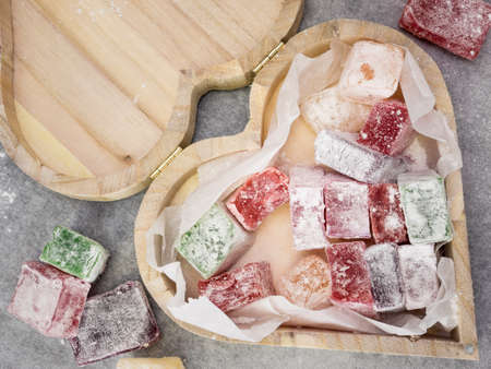 closeup of rustic heart shaped wooden box containing colourful turkish delight with turkish delight and gray work top behindの写真素材