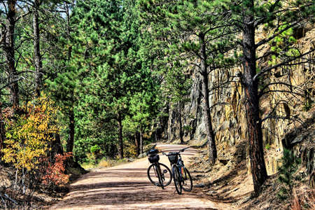 On an Autumn day in the mountains near Deadwood, SD, two bikes sit unoccupied on the George Mickelson State Trail surrounded by rocky cliffs and tall green pines.の写真素材