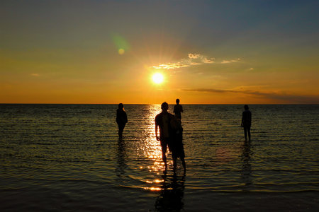 During low tide at Rock Harbor in Cape Cod Bay, a small group of young people, silhouetted and seen...