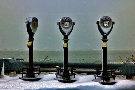 On a snowy winter's day on an ocean beach, three viewin g stations stand empty.