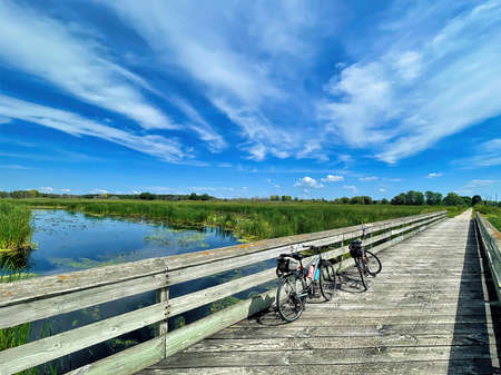 Beneath a partly cloudy blue sky on a summer day, two bikes rest against a railing on a wooden bridge passing over a stream on the Mascoutin Valley State Trail in Wisconsin.の写真素材