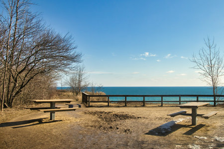 Wooden picnic tables and fence on the shore of Lake Michigan in early spring, atop a bluff at Lion's Den Gorge, near Grafton, WI.の写真素材