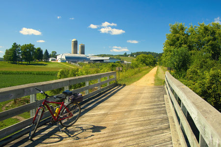 Rural landscape with a bicycle on a wooden bridge along the Elroy-Sparta State Trail with a farm in the distance on a Summer day near Sparta, WI.の写真素材