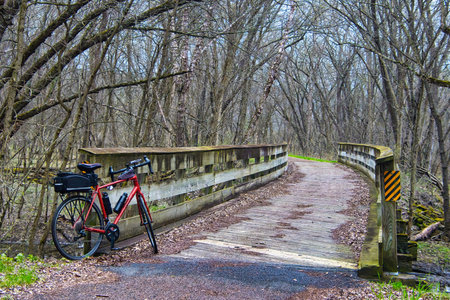 Closeup of a red bike beside a wooden bridge on a cloudy Spring day along the Chippewa River State Trail near Caryville, Wisconsin.の写真素材