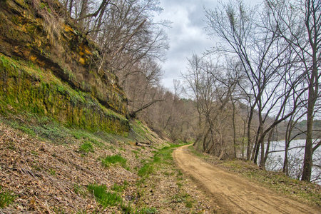 Early Springtime view of the Red Cedar Trail and River passing between rocky cliffs and the river in a forest of bare trees on a cloudy day near Menomonie, Wisconsin.の写真素材
