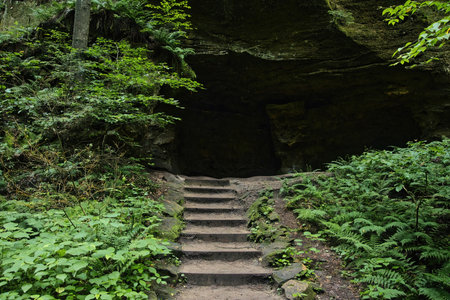 Overcast summer day closeup of rock steps leading to a dark cave along a trail at Hocking Hills State Park in Hocking County, Ohio.の写真素材