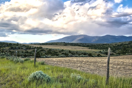 Landscape of distant mountains beyond a fenced in field on an overcast Summer day near Townsend in Broadwater County, Montana.の写真素材
