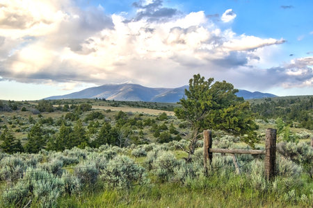 Landscape of distant mountains beyond a fence and rolling green hills on an overcast Summer day near Townsend, Montana.の写真素材