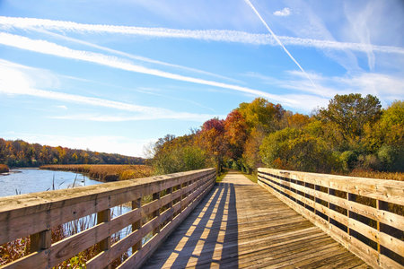 Beautiful Autumn view of the recreational trail crossing a river beneath a clear sky with many contrails near Merton, Wisconsin.の写真素材