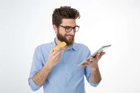 young man with brown hair and beard eats a snack at the officeの写真素材