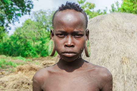 Omo River Valley, Ethiopia - November 29, 2020: Portrait of African Teenager with a big traditional wooden earrings in the local Mursi tribe villageのeditorial素材