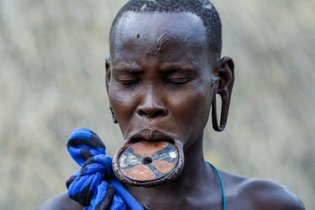 Omo River Valley, Ethiopia - November 29, 2020: Portrait of African Woman with a big traditional wooden plate in the lower lip in the local Mursi tribe villageのeditorial素材