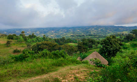 Breathtaking View to the Traditional African Houses, Green Trees and Mountains under Cloudy Blue Sky of the Omo River Valley, Ethiopiaの写真素材