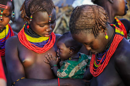 Omo River Valley, Ethiopian -November 30, 2020: Dassanech Tribe Woman in Traditional Bright Necklace with Little and Cute Infant on Hands in the Local Villageのeditorial素材