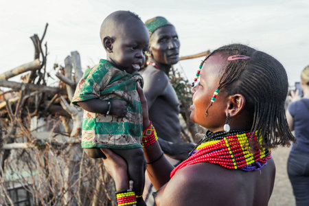 Omo River Valley, Ethiopian -November 30, 2020: Dassanech Tribe Woman in Traditional Bright Necklace with Little and Cute Infant on Hands in the Local Villageのeditorial素材