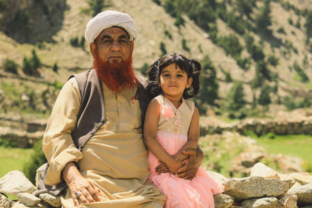 Gilgit, Pakistan - June 08, 2018: Old Man with Red Beard and Traditional Cap sitting near Little...