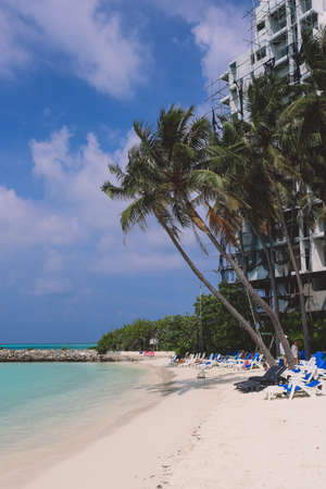 Maafushi, Maldives - June 25, 2021: People near the White Sandy Beach with the Palm Trees and Hotel Building on the Maldivian Paradise Islandのeditorial素材