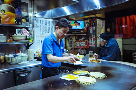 Local Cook preparing the Typical Japanese Dish Okonomiyaki in Hiroshima Restaurant, Japan