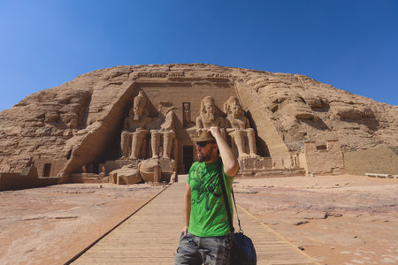 White Man Tourist in front of the Colossal Statues of Ramesses II seated on a throne near the entrance to the Great Temple at Abu Simbel, Egyptの写真素材