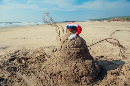 Funny Snowman in Sunglasses and Santa Red Hat, made of the Sand on Goa beach, Indiaの写真素材
