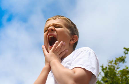 painful, hurting, screaming preteen boy against blue sky backgroundの写真素材