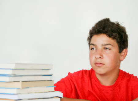 Daydreaming male teen with book stack to studyの写真素材