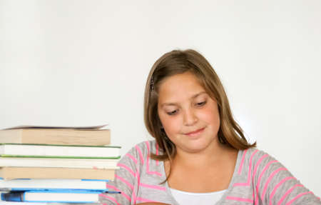 Perky, smiling preteen girl studying with book stackの写真素材