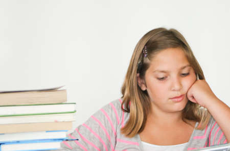 Bored-looking pretty preteen girl studying with book stackの写真素材