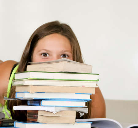 Playful teenage girl peeking over tall stack of booksの写真素材
