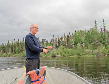 Retired old male fisherman with pole standing in boatの写真素材