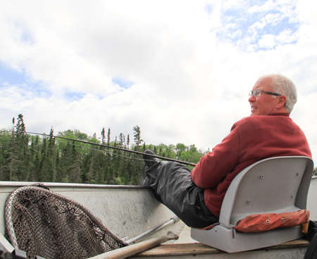 Retired old male fisherman with pole and net relaxing in boatの写真素材