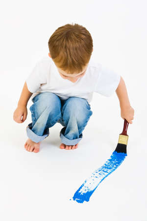 Three year old boy painting a big blue line on the floorの写真素材