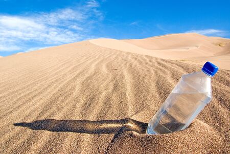 A cold bottle of water sitting in a sand duneの写真素材