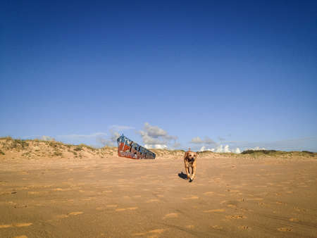 Stranded boat on the beach, painted with graffiti and a dog running in front of it.の写真素材