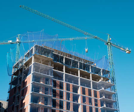 View of a residential building under construction in the city with cranes and safety netsの写真素材