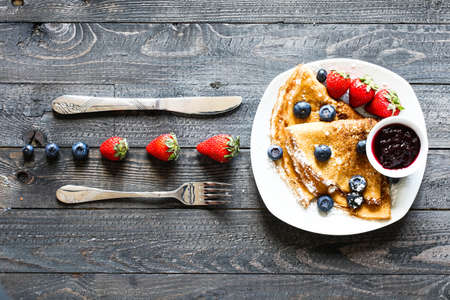 Delicious Crepes Breakfast with Dramatic light over a vintage wood background. An healthy meal of Pancakes with marmalede, blueberries and strawberries.の写真素材