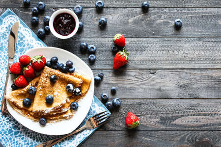 Delicious Crepes Breakfast with Dramatic light over a vintage wood background. An healthy meal of Pancakes with marmalede, blueberries and strawberries.の写真素材