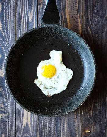 Fried egg in a black pan over a dark old dirty wood background with dramatic light.の写真素材