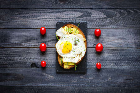 Delicious Tasty Avocado Eggs and Tomato Cheese Toasts over a stone plate with an old look wooden background and dramatic light.の写真素材