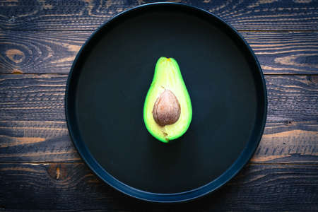 Veggie Food composition with half avocado over a darkdish and a wood distressed old background. Dramatic light.の写真素材