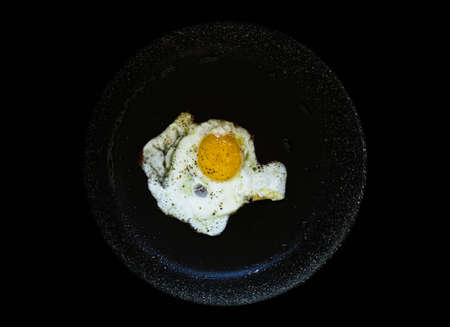 Fried egg in a black pan over a dark old dirty wood background with dramatic light.の写真素材