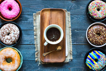 Colorful Donuts breakfast composition with different color styles of doughnuts and fresh coffee on the side over an aged wooden desk background.の写真素材