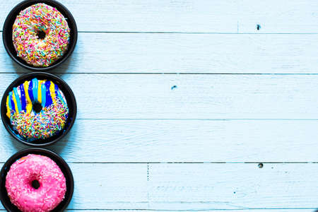Colorful Donuts breakfast composition with different color styles of doughnuts over an aged wooden desk background.の写真素材