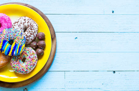 Colorful Donuts breakfast composition with different color styles of doughnuts over an aged wooden desk background.の写真素材