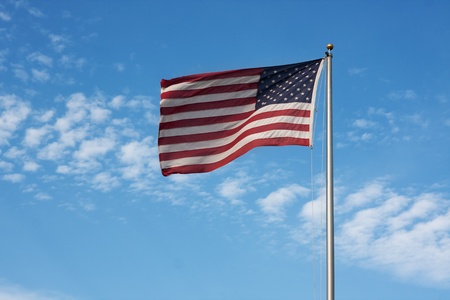 United States flag waves against a cloudy blue skyの写真素材